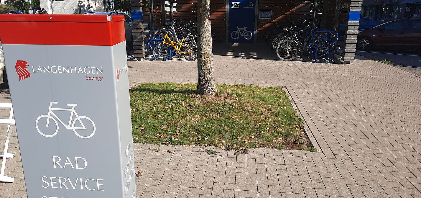 Mitte B+R mit Komfort! Vorne: Fahrrad-Reparaturstation, mit Pumpe, Werkzeug und Online-Instruktionen. - Im Hintergrund: Offener Abstellbereich