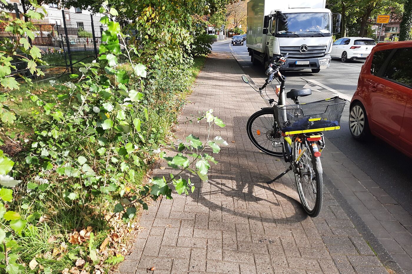 Typisch für die gefährliche Radwegesituation in Schulenburg: Ein kombinierter Zweirichtungs-Fuß- und Pflicht-Radweg von und zum Kindergarten und als Weg zur nächsten Grundschule: Dieser Weg ist deutlich schmaler als nach Vorschrift, nicht mal zwei Radfahrende können sich da begegnen, geschweige denn Radfahrende mit Kinderanhänger. Und jetzt ist er auch noch halb zugewachsen. Und gleich nebenan rollt der Verkehr ...