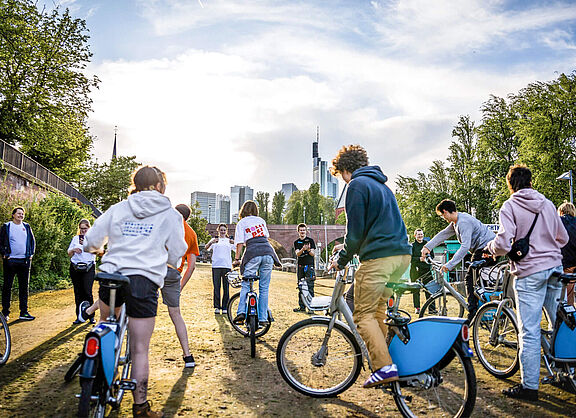 Junge Menschen fahren auf Leihfahrrädern auf einem Weg im Freien.