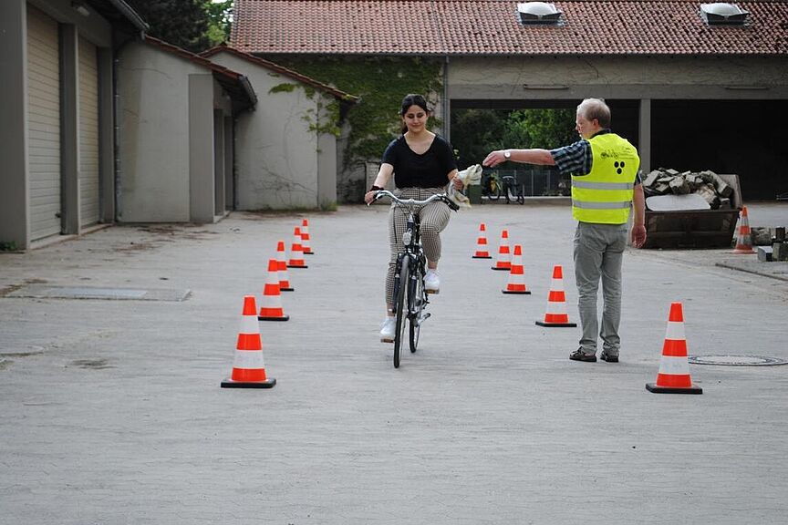 Übung Radfahrschule Frau fährt mit Fahrrad und nimmt Tuch von Lehrer entgegen