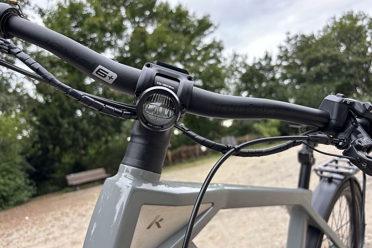 Großaufnahme eines am Lenker montierten, runden Scheinwerfers mit schwarzem Gehäuse an einem grauen Rad. 