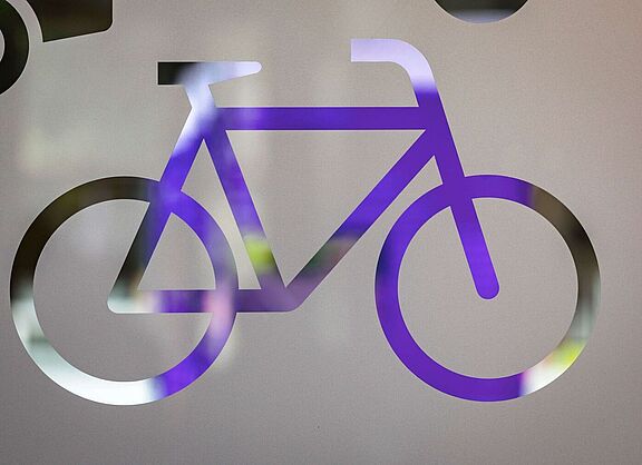 Lila Fahrradsymbol als durchsichtige Silhouette auf einer satinierten Glasfläche.